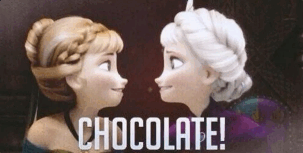 A still from the movie Frozen.

Features both sisters from the movie.

They are in a dark (reddish brown) panelled room, possibly with a throne and/or tapestries behind them.

Anna, on the left of the image, red hair in an up do with a braid crowing the front of her head, and wearing a sleeveless dress with a black choker, looks over her left shoulder toward...

Elsa, on the right of the image, white hair in an up do, the ends in a twist around the top of her head, a tiara positioned on top of it, wearing a dark purple cloak with a broach  holding it closed (we can't see her dress), looks over her right shoulder back toward Anna.

Both sisters are grinning widely at each other.

Below their faces, superimposed on the image, in white coloured font, we read:

CHOCOLATE!